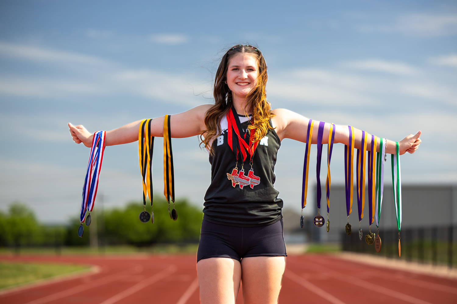 X• Prep track athlete on the track holding a season of medals, arms outstretched